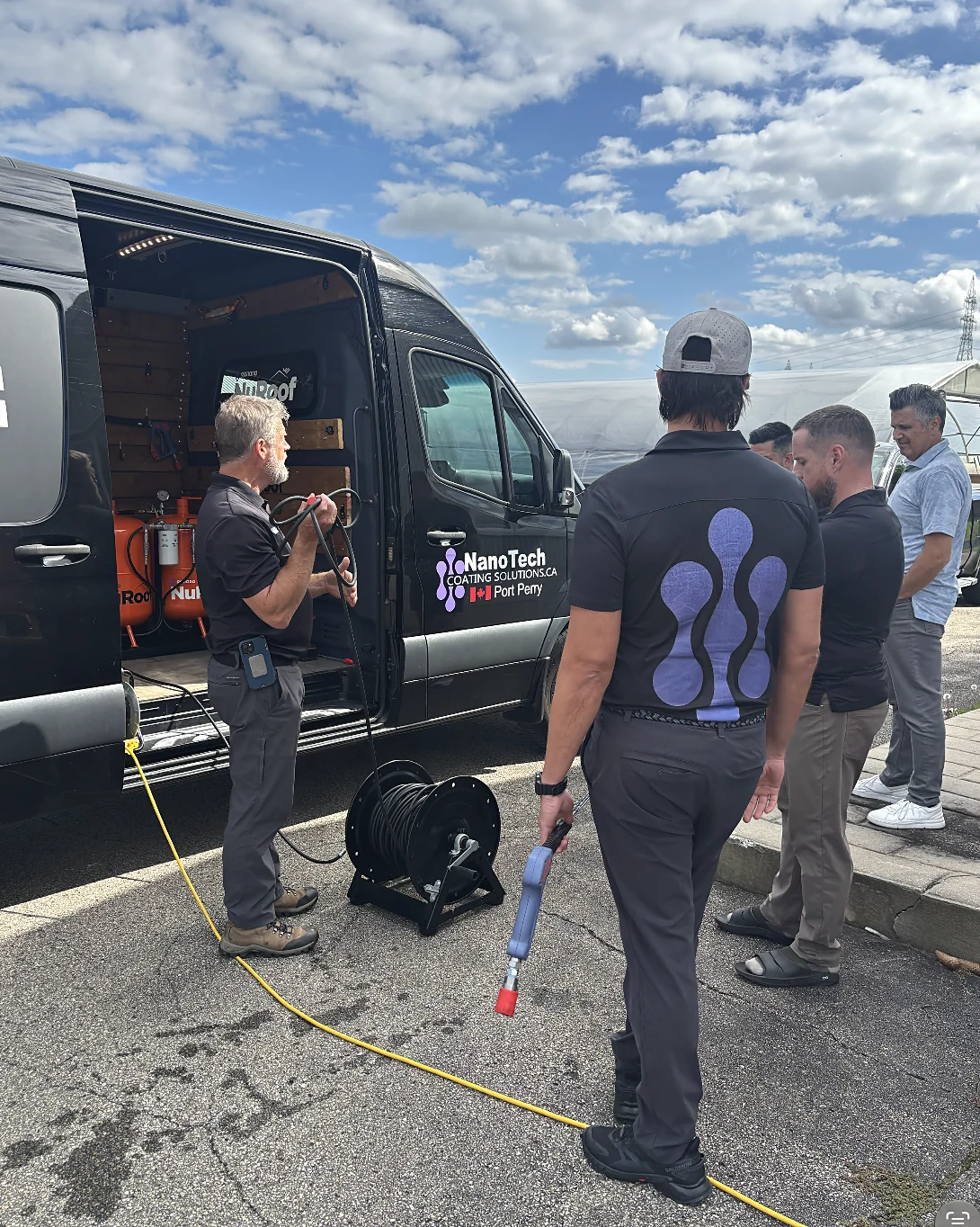 Steve demonstrating the hose reel and gun to a group of dealers beside the NanoTech van.