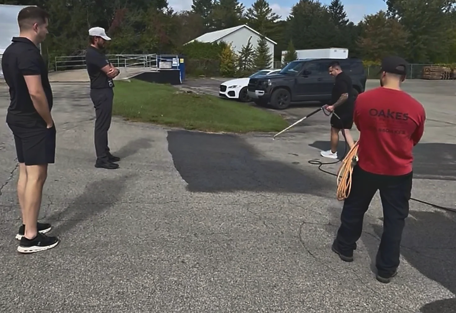 Dealers watching a demonstration in a yard, one spraying through a telescoping extension gun while another holds a coiled hose.