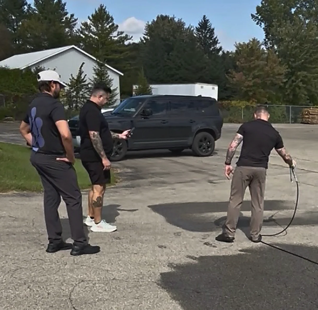 Dealers in a yard watching one of the group trigger the spray gun on the pavement.