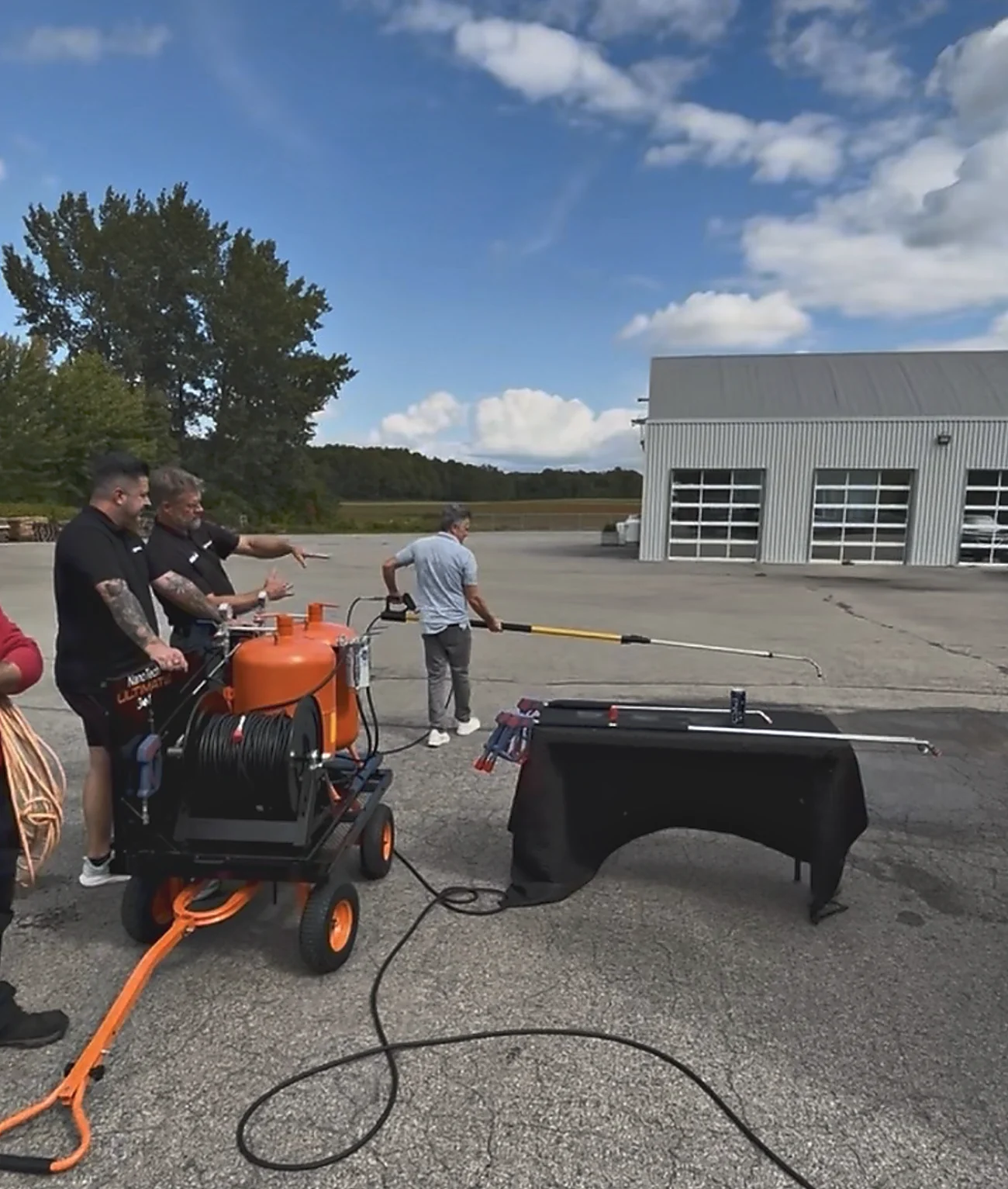 A demonstration in a yard: the Ultimate on its HD cart with the hose run out, while one of the group works a telescoping extension gun across the pavement.