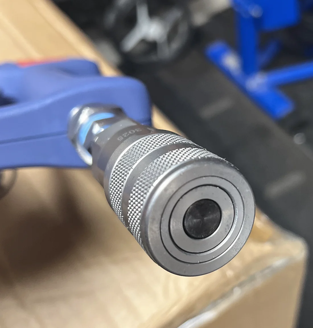 Close-up of a stainless steel quick connect fitted to the base of a blue trigger spray gun.