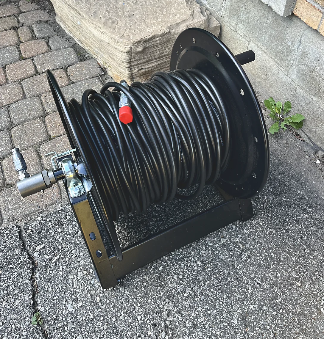 The removable hose reel standing on a driveway, wound with black hose and fitted with stainless quick connects.