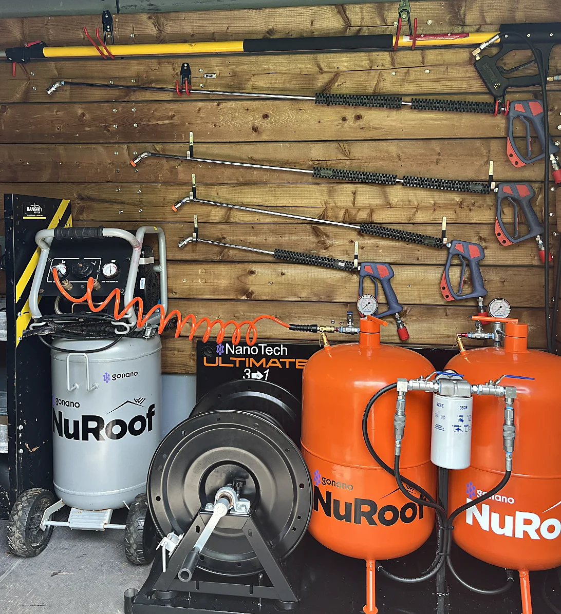 Shop wall hung with spray wands and trigger guns, with the compressor, reel and two orange NuRoof tanks below.