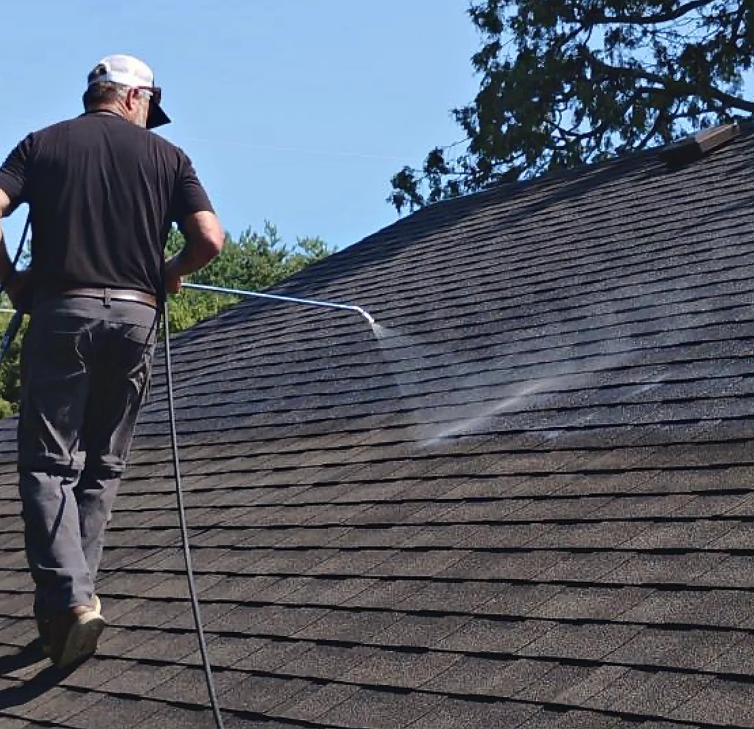 Applying coating across a shingle roof through a wand, hose trailing behind.